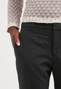 Pantaloni neri su misura con una texture liscia, dotati di tasche laterali e un design elegante. Indossati con un maglione a maglia con motivo.