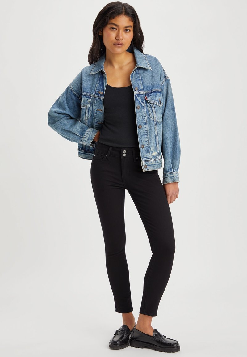Jeansjacke in hellblau mit lockerer Passform, kombiniert mit schwarzen Skinny-Jeans. Schwarze Loafers runden das Outfit ab. Einfaches Design, keine Muster.