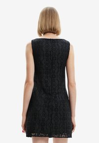 Black sleeveless dress featuring floral lace texture, fitted silhouette, and a back zipper closure, with a scalloped hem detail.