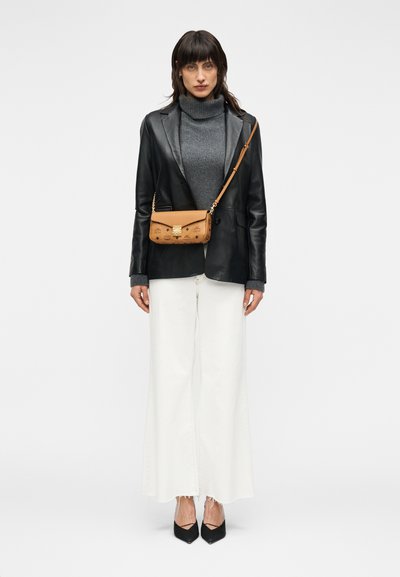 Γυναίκα που φοράει μαύρο δερμάτινο σακάκι, γκρι πουλόβερ με ζιβάγκο, άσπρο παντελόνι με φαρδύ μπατζάκι, μαύρες μυτερές γόβες και καφέ τσαντάκι χιαστί με χρυσό κούμπωμα.