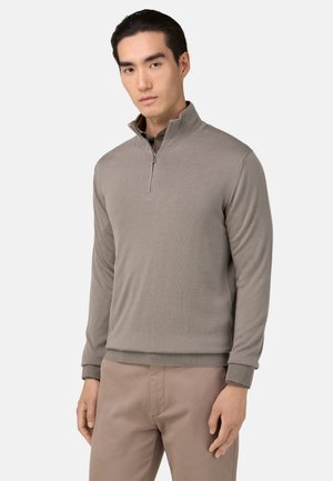 Sudadera de media cremallera en taupe claro con un patrón de punto texturizado y puños y dobladillo acanalados, combinada con pantalones beige claros.