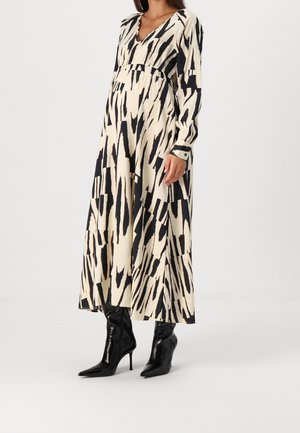 Long, cream dress with black abstract patterns, featuring a V-neck, long sleeves, and a fitted waist, paired with black stiletto boots.
