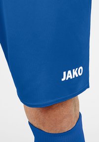 Blaue Sportshorts aus glattem Material mit einem weißen "JAKO"-Logo am unteren Saum. Das Design ist schlicht und athletisch.