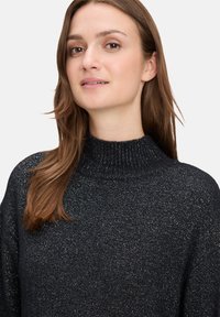 Pull col roulé noir pailleté avec un col côtelé. Texture douce et coupe décontractée, avec un léger éclat sur tout le tissu.