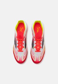 White and pink athletic shoes with black accents, textured upper, and bright yellow lining. Features flat laces and a tapered design.