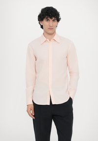 Lys ferskenfarvet langærmet skjorte med spids krave og knaplukning fortil, der har en lige pasform og glat, tekstureret stof.