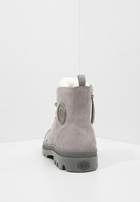 Hallutsina hallux, mis on valmistatud sametist, tekstureeritud kummist tallaga, sünteetilise karvkattega voodriga ning ringikujulise logo aktsendiga kandadel. Kaasas on tõmblukk.