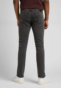 Jeans grigio scuro con taglio slim, cinque tasche e dettagli di cucitura visibili. Indossati con sneakers bianche. Design semplice, senza motivi prominenti.