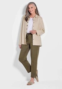 Veste beige à boutons, chemise blanche, pantalon vert olive avec fentes sur les côtés et sandales beige clair. Coupe lisse, décontractée et design casual.
