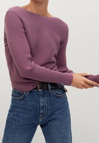 Maglione a coste di colore viola tenue con scollo ampio e maniche aderenti, abbinato a jeans di denim blu a vita alta e una cintura nera.