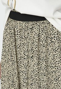 Pleated skirt in beige fabric with a black animal print pattern, featuring a black elastic waistband for comfort and fit.