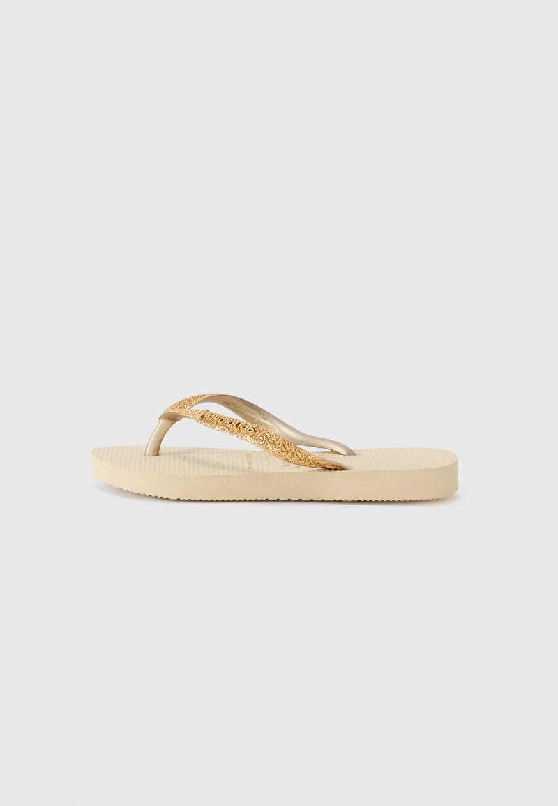 Šlepetės su smėlio spalvos tekstūruotu padu ir auksiniu blizgiu dirželiu. Plokščias padas su grioveliais, užtikrinančiais sukibimą. Paprastas dizainas, lengvas medžiagos.