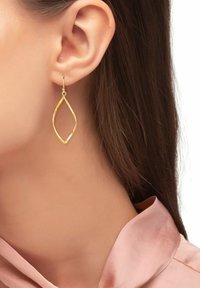 Pendientes de metal en tono dorado con un diseño en forma de hoja, que presentan una superficie lisa y un contorno delgado, que cuelgan de un gancho sencillo.