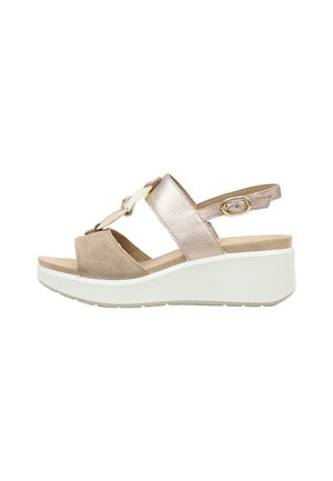 Sandalia de cuña beige y metálica con correa ajustable en el tobillo y cadena decorativa en la parte delantera sobre suela blanca.