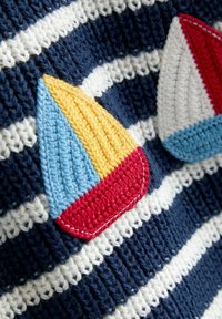 Tissu rayé bleu marine et blanc avec des appliqués de voiliers brodés en fils rouges, jaunes et bleus, avec des détails texturés.