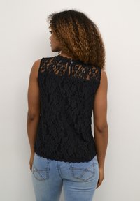 Haut sans manches en dentelle noire avec un décolleté festonné et une fermeture à bouton dans le dos. Assorti à un jean en denim bleu clair.