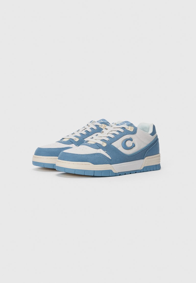 Blå och vita sneakers med övre del av canvas, gummisula, rund tå och framträdande cirkulär logo på sidan. Snörningarna är ljusbeiga.