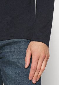 Camicia a maniche lunghe blu navy con una texture a coste, design aderente e orlo naturale, abbinata a jeans in denim blu strappati.