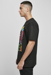 Camiseta negra de algodón con gráfico de texto multicolor en la parte frontal, mangas cortas y un corte relajado. Parte posterior lisa sin detalles adicionales.