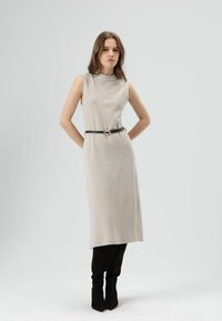 Knielange, lichtbeige jurk met mouwloos ontwerp, gestructureerde stof, opgesnoerd met een donkerbruine riem met een ovale gesp.