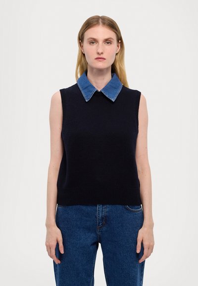 Mouwloze marineblauwe gebreide trui met een denim kraag. Heeft een geribbelde zoom en is gecombineerd met hoge taille blauwe jeans. Eenvoudig ontwerp.