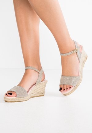 Sandales à talons compensés avec un empiècement supérieur en tissu doré texturé, une conception à bout ouvert et une sangle de cheville avec une boucle dorée. Talon compensé style liège.