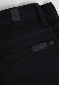 Svarta denimbyxor med en jämn textur, försedda med en baketikett, bältesöglor och kontrasterande sömmar längs sömmarna.