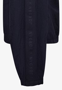 Pantaloni da jogging blu navy con polsini elasticizzati, caratterizzati da una striscia testurizzata con il logo "JORDAN" lungo il lato. Realizzati in materiale leggero.