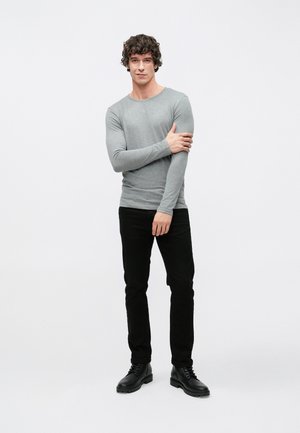 Grijs langarmig shirt gemaakt van zachte stof, gecombineerd met zwarte broek en zwarte enkellaarsjes, met een losse pasvorm en een ronde hals.