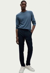 Hellblauer Pullover mit gerippter Textur, kombiniert mit navyblauen Hosen und weißen Sneakers. Das Outfit zeichnet sich durch eine schlanke Passform und ein minimalistisches Design aus.