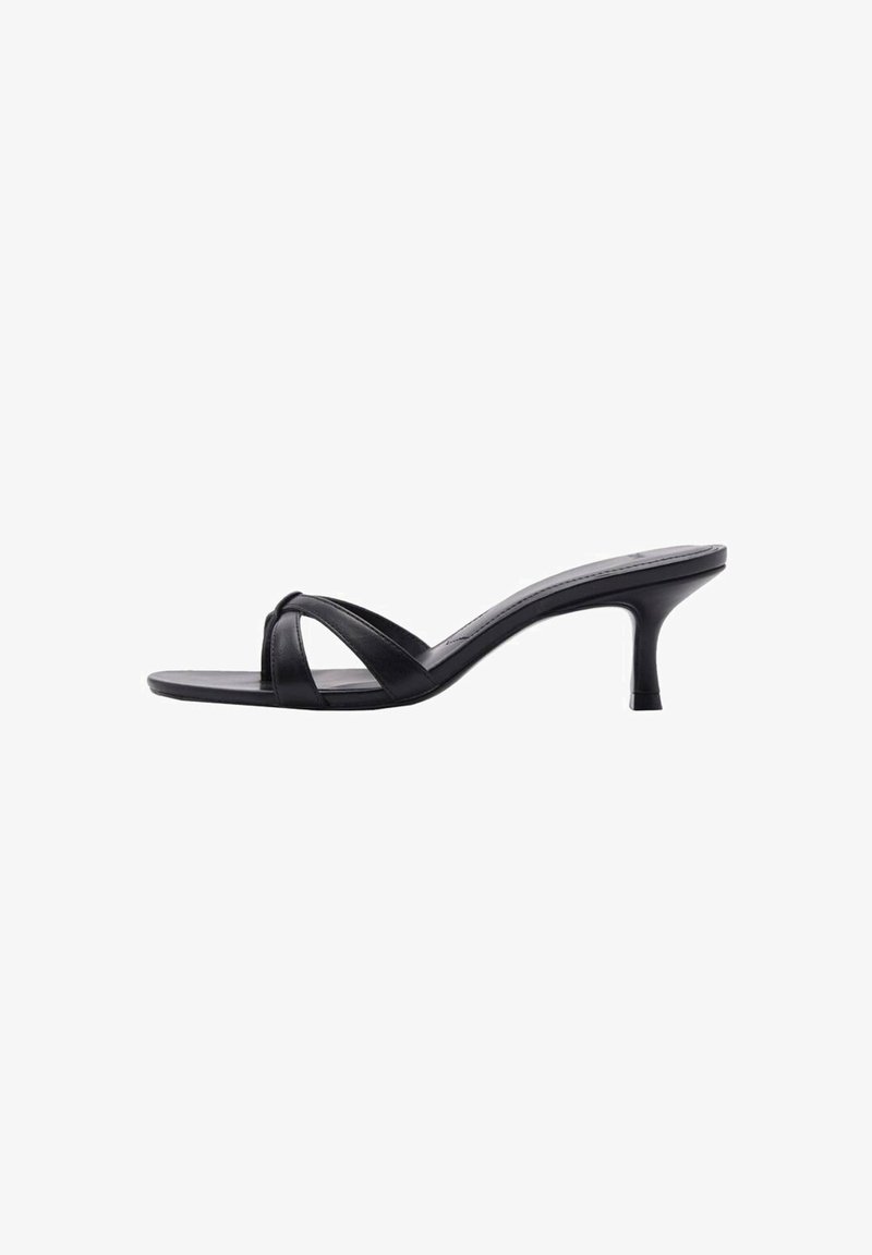 Sandalia de tacón de cuero negro con diseño de tiras cruzadas, punta abierta y tacón de aguja estilizado. Textura suave y estilo minimalista.