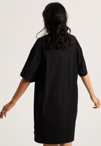 Robe t-shirt noire surdimensionnée, manches courtes, encolure ronde, en coton doux, ourlet légèrement plus long à l'arrière, design simple, sans motifs.