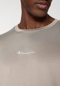 Φωτεινό μπεζ εφαρμοστό t-shirt με κοντά μανίκια και στρογγυλή λαιμόκοψη, με λευκό λογότυπο "Champion" στο στήθος. Λεία υφή.