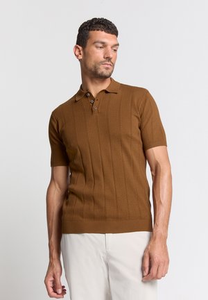 Bruine gebreide polo met korte mouwen, voorzien van een gestructureerd patroon en een knoopsluiting met drie knopen. Gecombineerd met lichte broek.