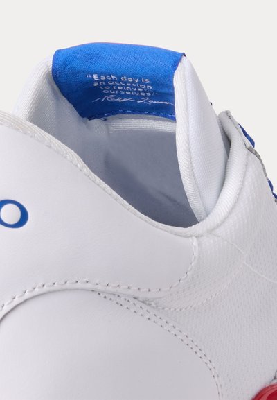 Sapatilha branca desportiva com detalhes em azul e vermelho. O interior apresenta uma língua azul com uma citação impressa. Textura suave, forma arredondada.