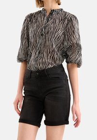 Černobílá zebra pruhovaná průhledná blůza s vysokým stojáčkem a zapínáním na knoflíky, spárovaná s černými denimovými šortkami s vysokým pasem.