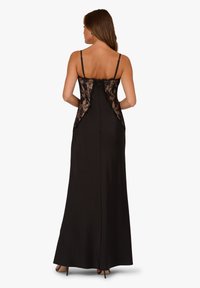 Abito da sera nero con spalline sottili, dettagli in pizzo sulla schiena e una silhouette liscia che arriva fino a terra.