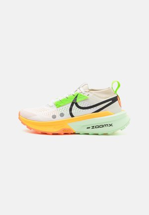 Biało-neonowo-zielony but do biegania Nike ZoomX z pomarańczową podeszwą, czarnym znakiem Swoosh i pętelką na białym tle.