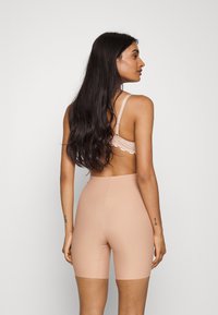 Nude høyhalsede shapewear-shorts med en glatt, elastisk tekstur, som har en tettsittende silhuett og minimale sømdetaljer.