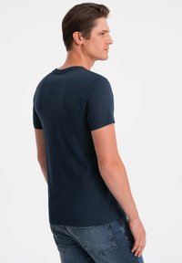 Tmavě námořnická modrá krátkosrstá tričko s kulatým výstřihem, s hladkou texturou a přiléhavým tvarem, nošené s světlými džínami.
