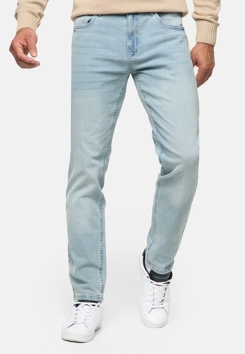 Jeans de mezclilla azul claro con un corte recto, diseño de cinco bolsillos y un ligero desvanecimiento. Combinados con zapatillas blancas para un contraste.
