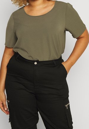 Top verde oliva a maniche corte con scollo rotondo, abbinato a pantaloni cargo neri a vita alta con tasche con zip.