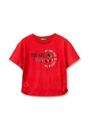 Camiseta roja de manga corta con los laterales fruncidos, cerezas estampadas y texto que dice "ERES cereza" y texto circular "RY-ISH THE LITTLE 65".