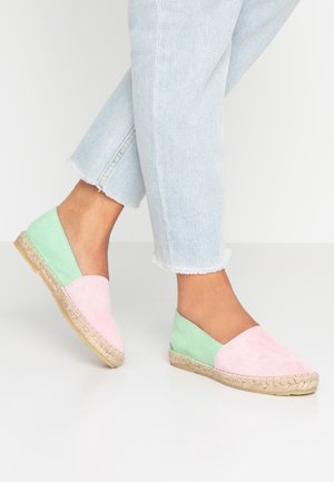 Espadrilles de ante con un diseño de bloques de color rosa y verde, que presentan una suela de yute trenzado y una forma plana, llevadas con jeans cortos.