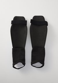 Zwarte beschermende scheenbeschermers met rubberen lichaam, korte mouwen en verstelbare banden voor een stevige pasvorm. Gladde oppervlakte met een matte afwerking.