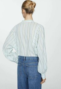 Witte en lichtblauwe gestreepte blouse met pofmouwen, gecombineerd met hooggepaste blauwe jeans. De stof lijkt licht van gewicht en heeft een gestructureerde textuur.
