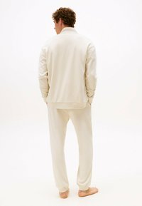 Ensemble de vêtements d'intérieur beige comprenant un haut à manches longues avec col et un pantalon assorti. Texture douce et lisse avec des poignets et une taille élastiques.