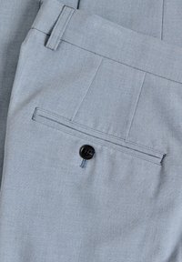 Pantalones gris claro con un bolsillo trasero con un botón negro, diseño con pliegues y textura suave.