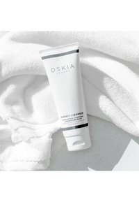 Oskia London Perfect Cleanser i en vit tub med svart text och accenter, vilande på en strukturerad vit handduk. Slät, ren design.