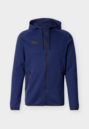 Mörkblå zip-hoodie med svarta dragsnören, framfickor med dragkedja och en subtil varumärkeslogotyp på vänster bröst.